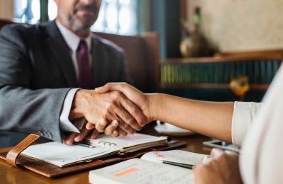 A lawyer and client shake hands over the attorney's desk.